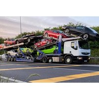 White truck transporter carrying multiple cars on a highway, featuring a blue and green trailer.