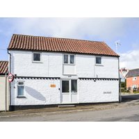 White two-story cottage with red-tiled roof, small front windows, and a central door, located on a street corner.