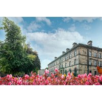 Historic stone hotel with classic architecture, surrounded by lush greenery and vibrant pink flowers under a blue sky.
