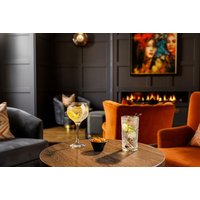 Cozy hotel lounge with dark walls, orange chairs, a lit fireplace, and drinks on a wooden table.
