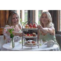 Two women enjoying afternoon tea with a three-tiered stand of pastries and sandwiches, set on a white tablecloth.