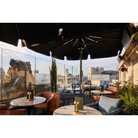 Rooftop terrace with round tables, black umbrellas, city view, and plush seating at The Rex, formerly Hotel Gotham.