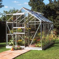 Green metal-framed greenhouse with clear panels, pitched roof, and sliding door, set on grass with plants inside.