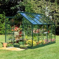 Green-framed greenhouse with large paned toughened glass, filled with plants, set on a grassy lawn.