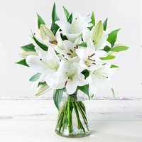 Casablanca Lily Bouquet with white lilies, green leaves, and buds in a clear glass vase.