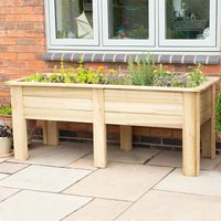 Wooden rectangular planter box on legs, filled with plants, against a brick wall and window.