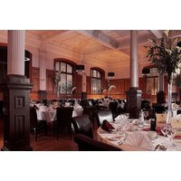 Elegant dining room with round tables, white tablecloths, tall floral centerpieces, and large windows at The Crown Hotel.