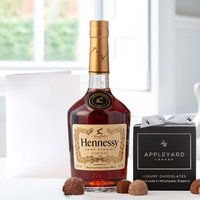 Hennessy bottle with gold label, box of 12 handmade chocolate truffles, and a blank occasion card on a table.