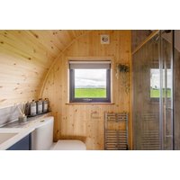 Wooden glamping pod interior with window view, modern bathroom fixtures, and glass shower in Cumbria countryside.