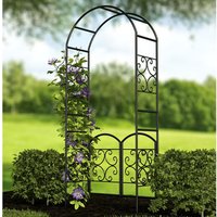 Black metal garden arch with scroll design and gate, 7'5" tall, surrounded by greenery and flowers.
