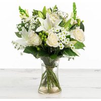 White rose and lily bouquet in a clear vase with greenery and small white flowers.