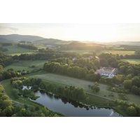 Tinto Hotel surrounded by lush green landscape, with a serene pond and rolling hills in the background.