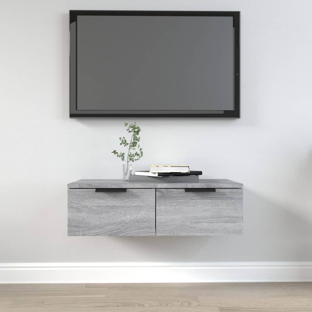Grey Sonoma wall cabinet made of engineered wood, featuring two drawers and a minimalist design, mounted below a flat-screen TV, with a small plant and books on top.