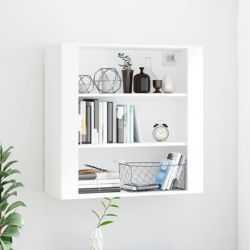 White wall cabinet made of engineered wood, featuring three open shelves displaying books, decorative items, and a wire basket, set against a light wall with greenery.