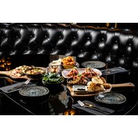 Dining table with assorted dishes, wine glasses, and beer on a glossy black surface, surrounded by tufted leather seating.