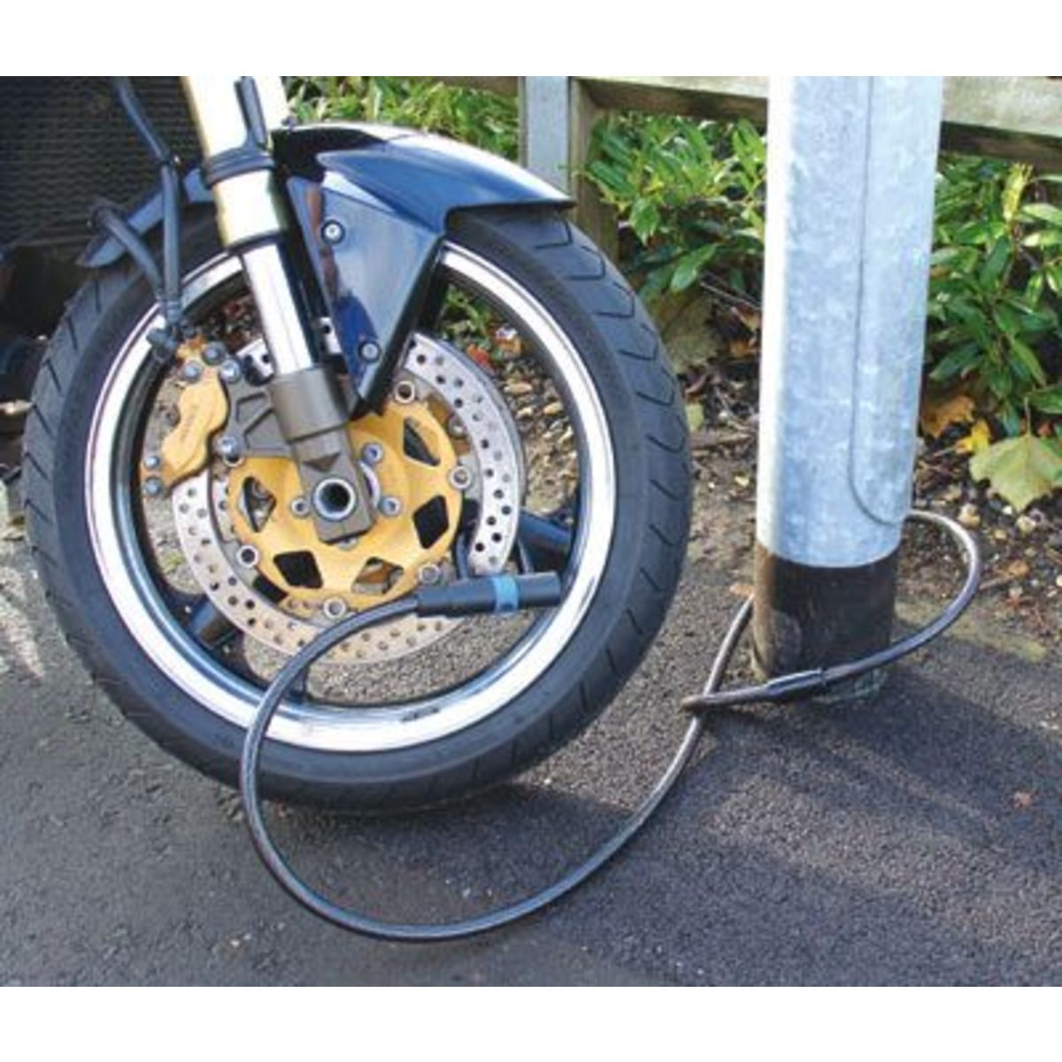 Black Mammoth Security Loop & "U" Cable Lock secured to a motorcycle wheel, with a sturdy metal construction and a coiled cable looped around a metal pole.