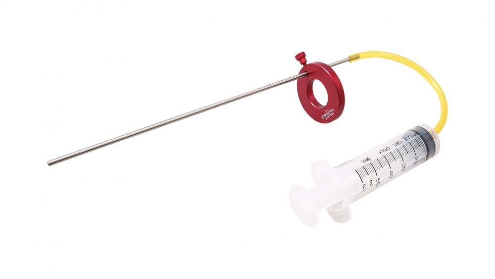 Red metal gauge with a circular opening, attached to a clear plastic syringe marked with measurements, and a yellow flexible tube for measuring motor bike oil levels.