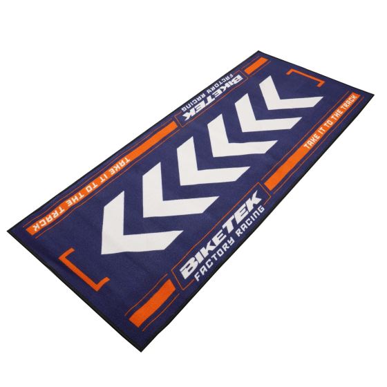 Blue carpet with bold white chevron patterns and orange accents, featuring "BikeTek Factory Racing" text, designed for environmental use and durability.