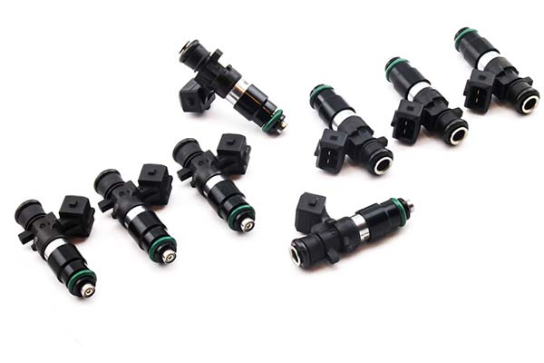 Set of 8 DeatschWerks 1200cc fuel injectors featuring black and green plastic bodies, metal tips, and electrical connectors, designed for 03-06 Mercedes CL55 AMG and E55 AMG.