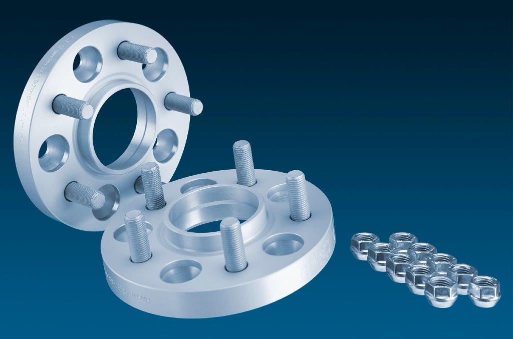 Silver aluminum H&R 5065673 TRAK+® wheel spacers, 25mm thick, featuring five holes and accompanying lug nut covers, against a dark blue background.