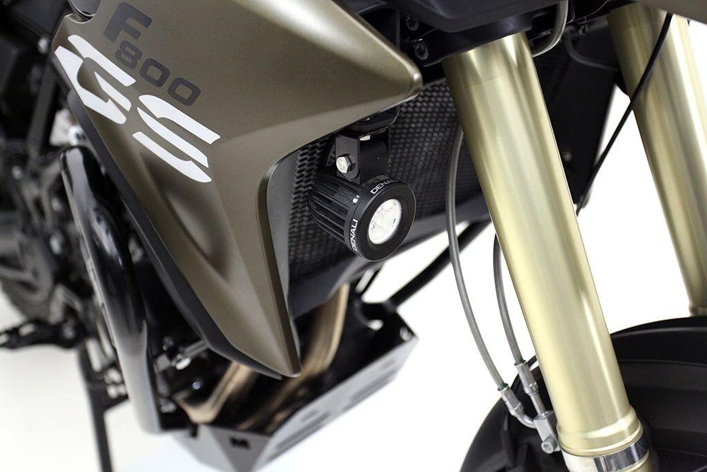 Denali BMW F800GS/Adventure lighting mount in black and silver, featuring a round LED light, mounted on a textured surface with gold-colored fork tubes.