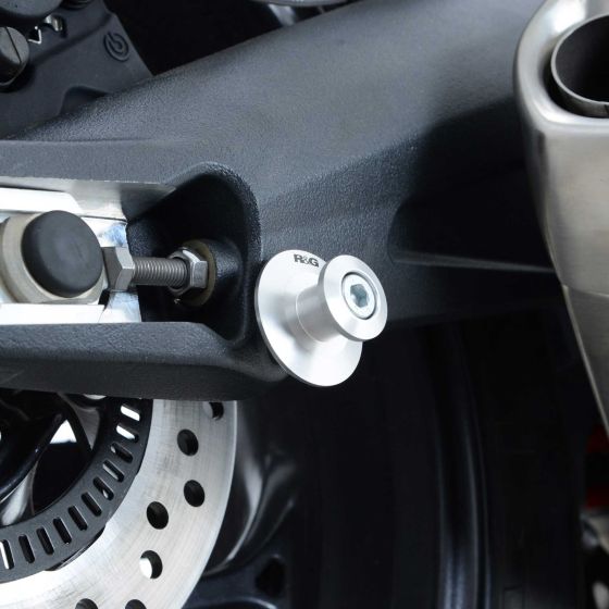 Silver 8mm elevation paddock stand bobbins by R&G, featuring a sleek aluminum design, securely attached to a motorcycle swingarm near the brake disc.