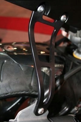 Black metal motorcycle exhaust hanger with a sleek, curved design and multiple cutouts, featuring silver mounting screws, attached near a tire.