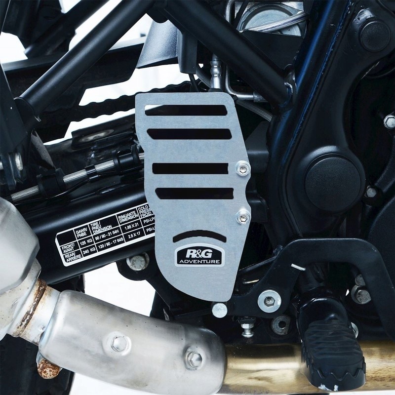 Silver aluminum engine cover with slotted design, featuring R&G branding, mounted on a motorcycle frame near the exhaust pipe and gear lever.
