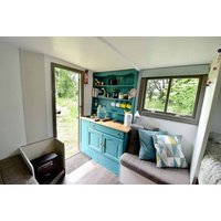 Cozy interior of Romany caravan with teal kitchenette, sofa, and window view of greenery.