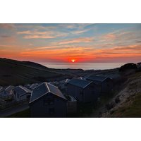 Caravans at Woolacombe Sands Holiday Park with ocean view, nestled among rolling hills under a vibrant sunset sky.
