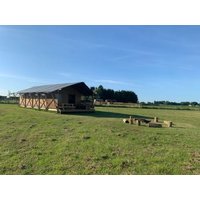 Large canvas safari tent with wooden deck on grassy field under clear blue sky.