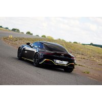 Black Aston Martin Vantage on a racetrack, sleek design, tinted windows, yellow accents, and dual exhaust.
