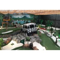 Jungle-themed adventure golf course with zebra-striped jeep, tropical plants, rocks, and artificial turf pathways.