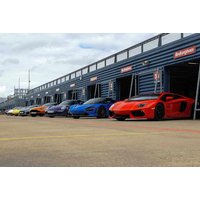 Row of colorful supercars including red, blue, and orange parked in front of a garage at a driving experience location.