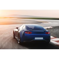 Blue sports car on a racetrack at sunset, sleek design with rear spoiler and dual exhaust.