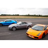 Blue sports car, silver convertible, and orange supercar parked on a racetrack with grassy fields in the background.