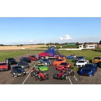 Supercars in various colors parked on a racetrack, including red, blue, green, and orange models, with a truck in the background.