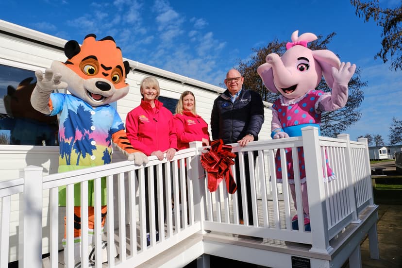 Brightly colored mascots stand with smiling staff on a deck of a modern respite home in Primrose Valley, under a clear blue sky.
