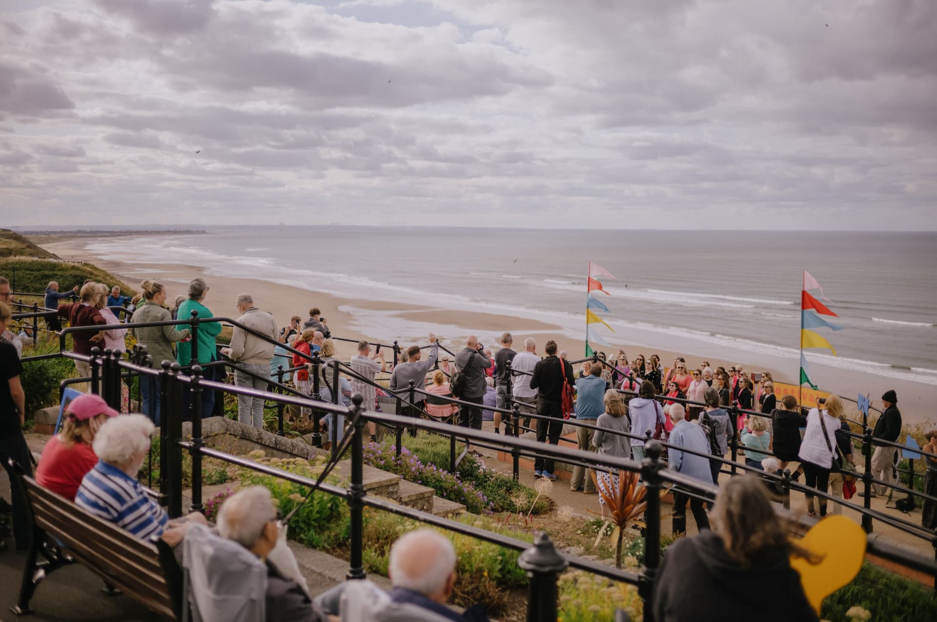 Crowd enjoying seaside view from cliff top with flags in Yorkshire