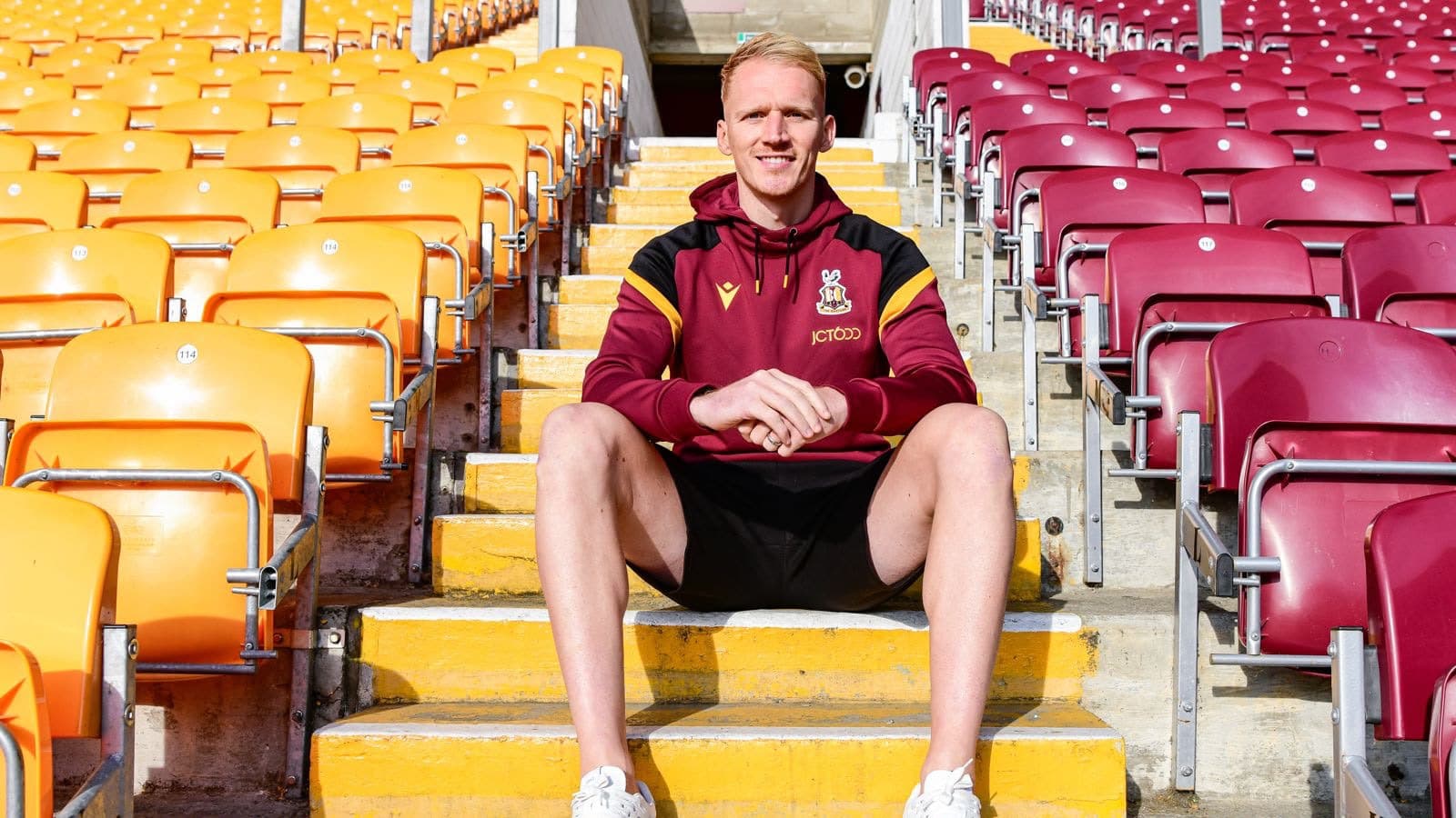 Man in maroon sports hoodie sitting on yellow stadium steps
