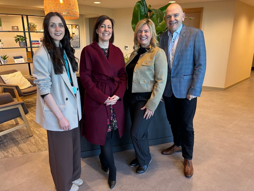 Four professionals stand together in a modern office setting, smiling and dressed in smart attire, promoting community support.