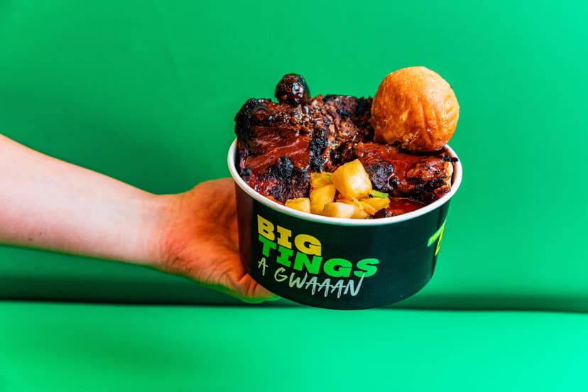 Hand holding Caribbean food bowl with grilled meats and plantains
