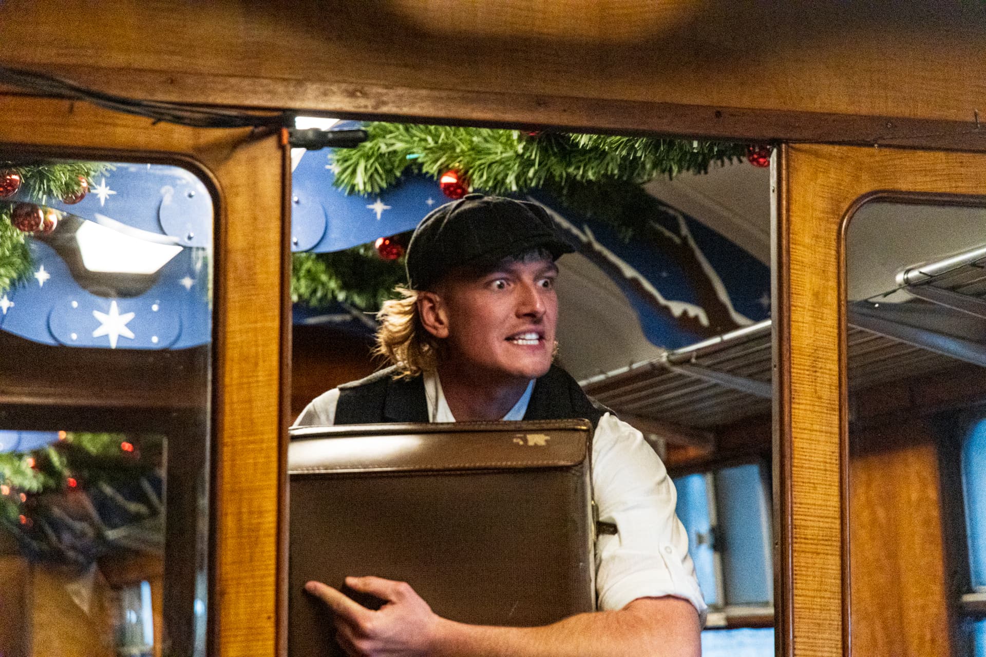 Man in vintage train carriage holding suitcase with festive decor