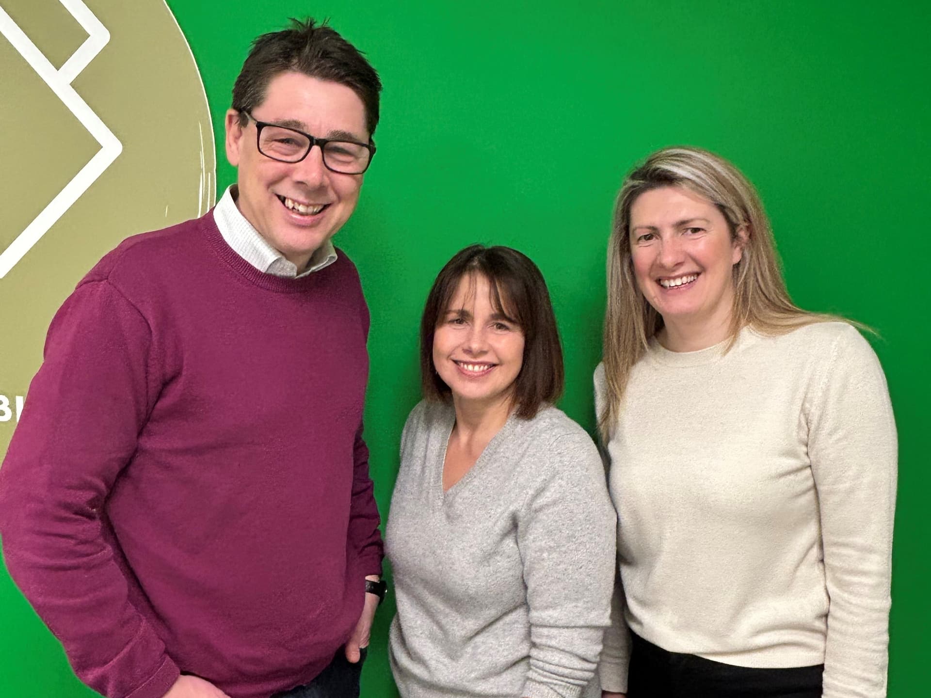 Three smiling people standing against a green wall