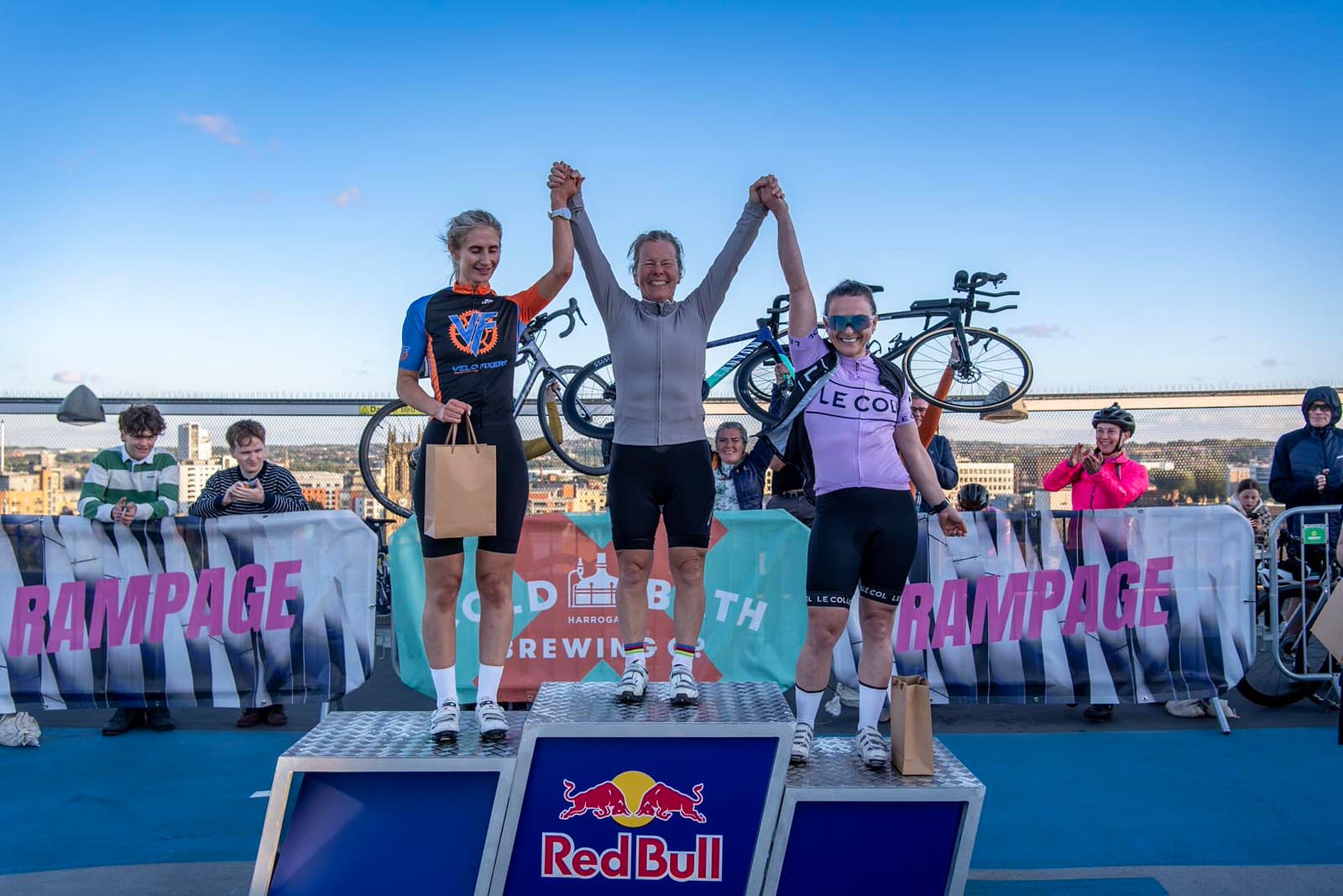 Cyclists on podium at outdoor event with cheering crowd