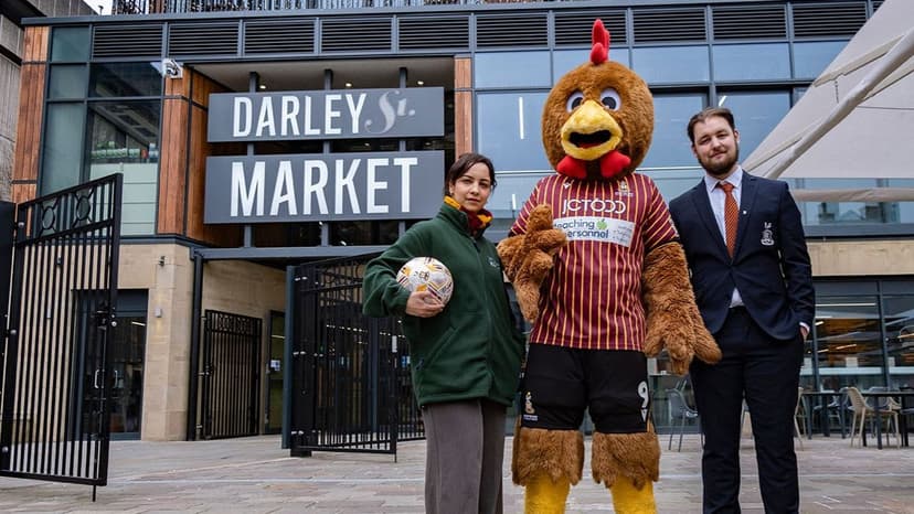Three people, including a mascot, outside Darley St Market