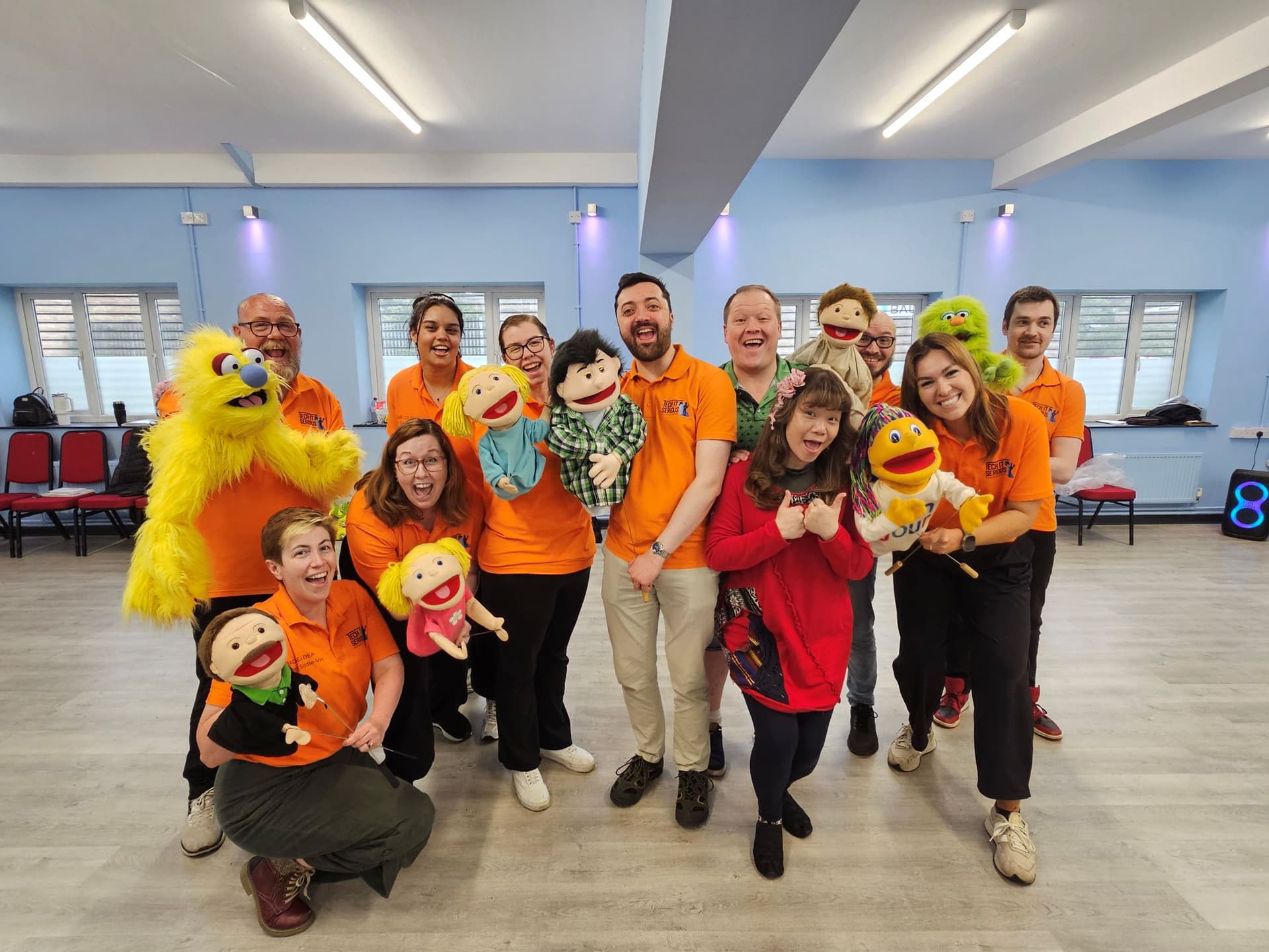 Group of people holding colorful puppets in a bright room