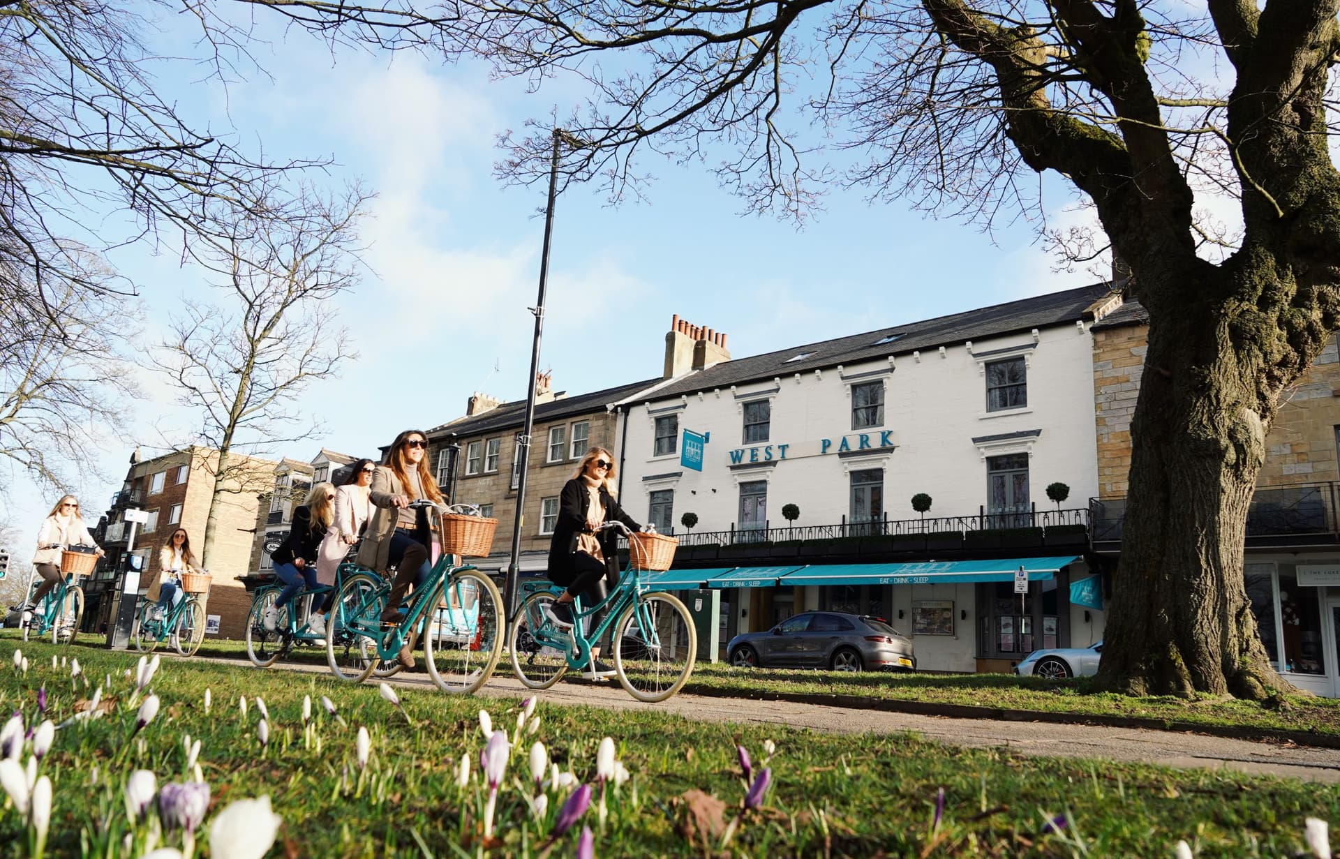Cyclists ride past historic West Park building under clear sky