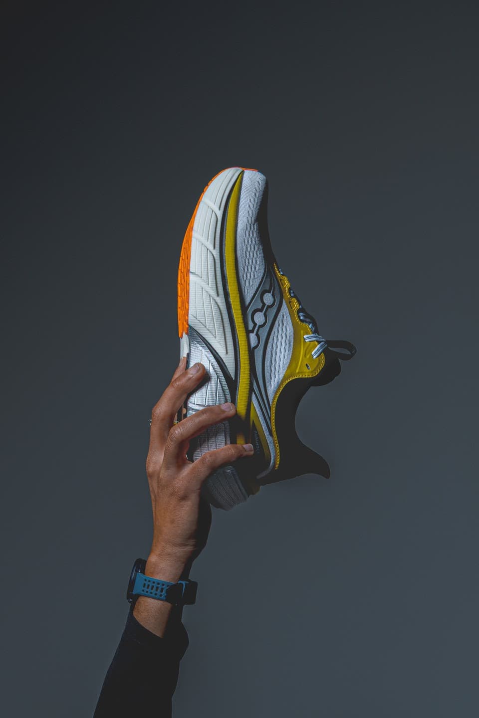 Hand holding yellow and white running shoe against dark background