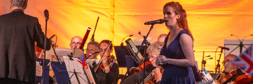 Singer in blue dress performing with orchestra under warm lighting
